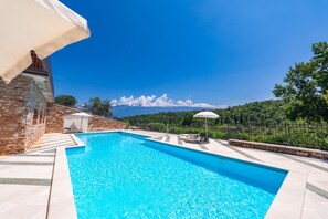 A swimming pool with a stone wall and a white umbrella, surrounded by a stone fence and greenery. - Residence Albatros A1 by Wonderful Italy (Toscolano Maderno)