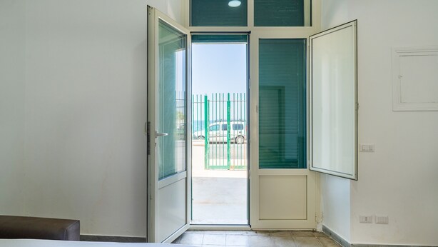 A room with a bed, a door leading outside, and a view of a vehicle through the door. - The Sea Outside Apartment 01 by Wonderful Italy (Bari)