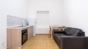 A compact kitchen with a white countertop, a built-in oven, and a white refrigerator. There is a black leather sofa and a wooden dining table with chairs. - The Sea Outside Apartment 01 by Wonderful Italy (Bari)