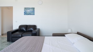 A hotel room with a bed, a leather sofa, a painting on the wall, and a nightstand with a lamp. - The Sea Outside Apartment 02 by Wonderful Italy (Bari)