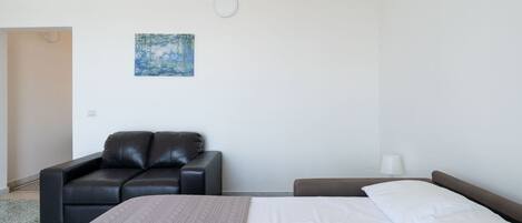 A hotel room with a bed, a leather sofa, a painting on the wall, and a nightstand with a lamp.