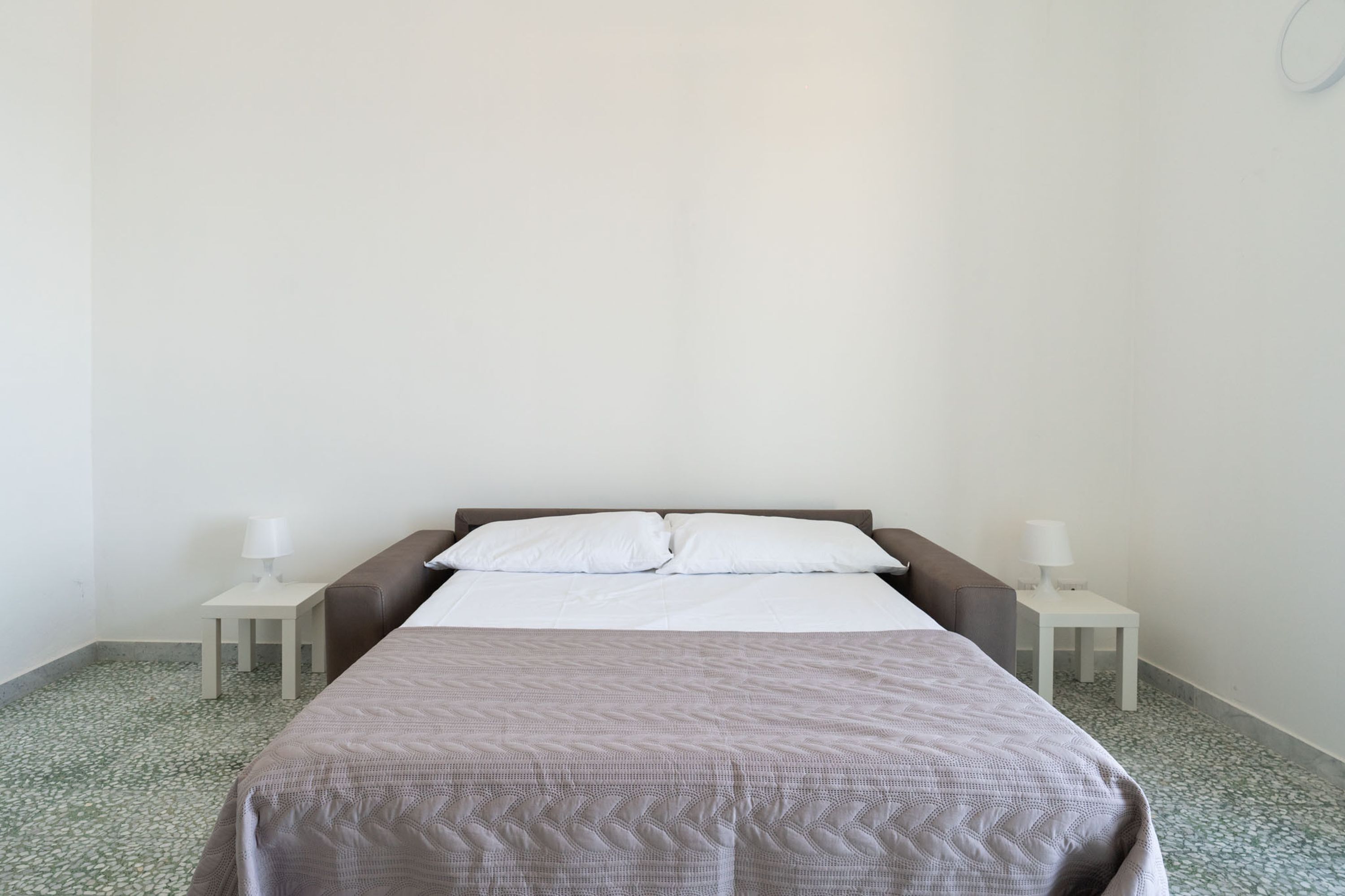 A simple, clean room with a bed, two bedside tables with lamps, and a tiled floor.