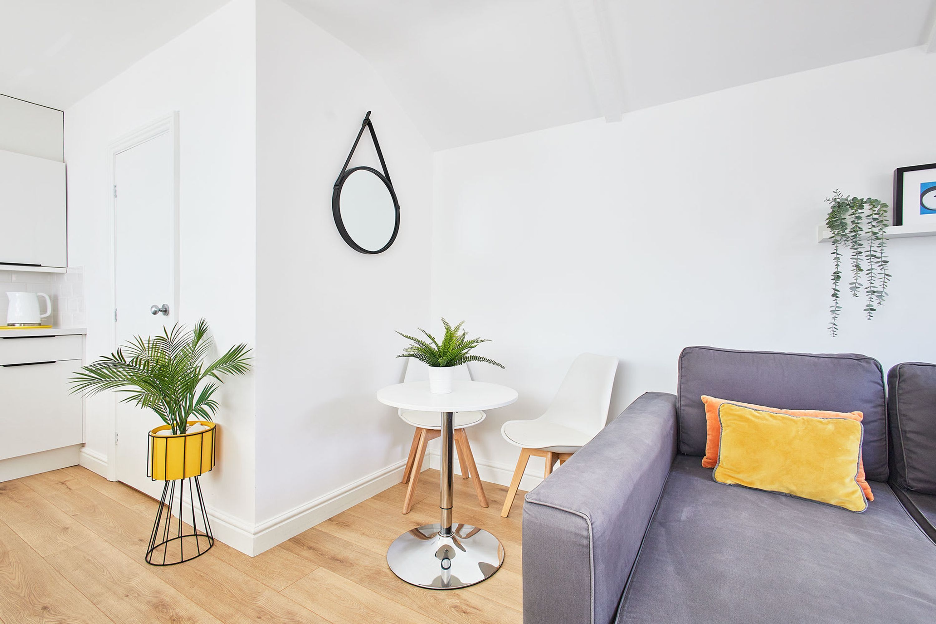 A modern living room with a grey sofa, a small white table, and a yellow plant stand.