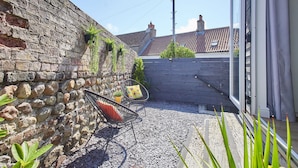 A patio area with a stone wall, a metal chair, and a wooden fence. - Host Stay Sunnyside Studio (Bridlington)