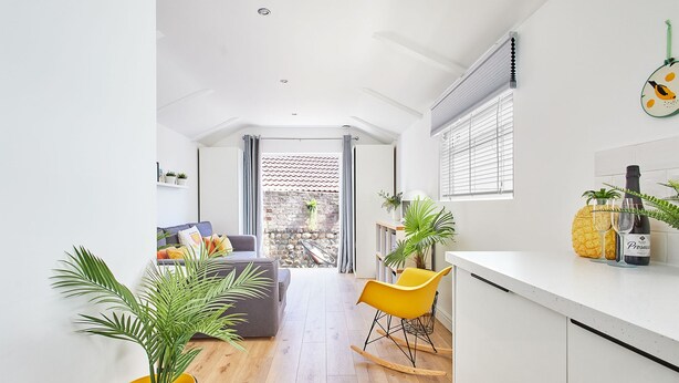 A modern, bright living room with a wooden floor, a yellow rocking chair, and a dining area with a white countertop and potted plants. - Host Stay Sunnyside Studio (Bridlington)