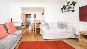 Ein modernes Wohnzimmer mit einem grauen Sofa, einem weißen Sofa und einem roten Teppich. Im Hintergrund befindet sich ein Essbereich mit Tisch und Stühlen.