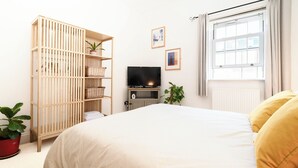 Ein Schlafzimmer mit einem Bett, einem Fernseher auf einem Schrank, einem Babybett und einem Fenster mit Vorhängen.