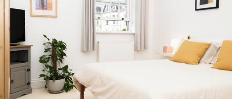 A bedroom with a bed, a potted plant, a radiator, a television, and framed artwork on the wall.