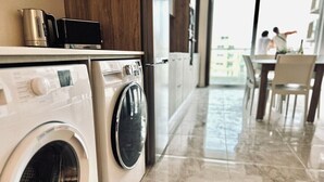 A modern kitchen with a washing machine and dryer, a coffee maker, and a dining area with a view.