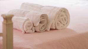Cama bem arrumada com toalhas brancas dobradas e cabeceira de madeira.
