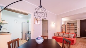 A dining area with a wooden table, chairs, a decorative vase, a red sofa with patterned cushions, and a geometric pendant light. - Casa Petroni in Bologna (Bologna)