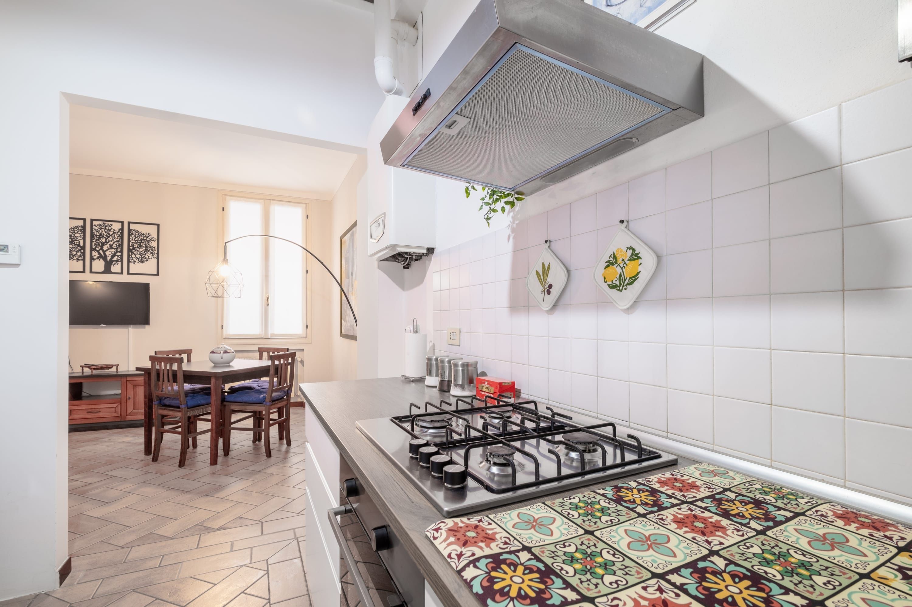 Une cuisine équipée d’une cuisinière à gaz, avec des murs recouverts de carreaux blancs, un coin repas comprenant une table et des chaises, et des carreaux décoratifs sur les murs.