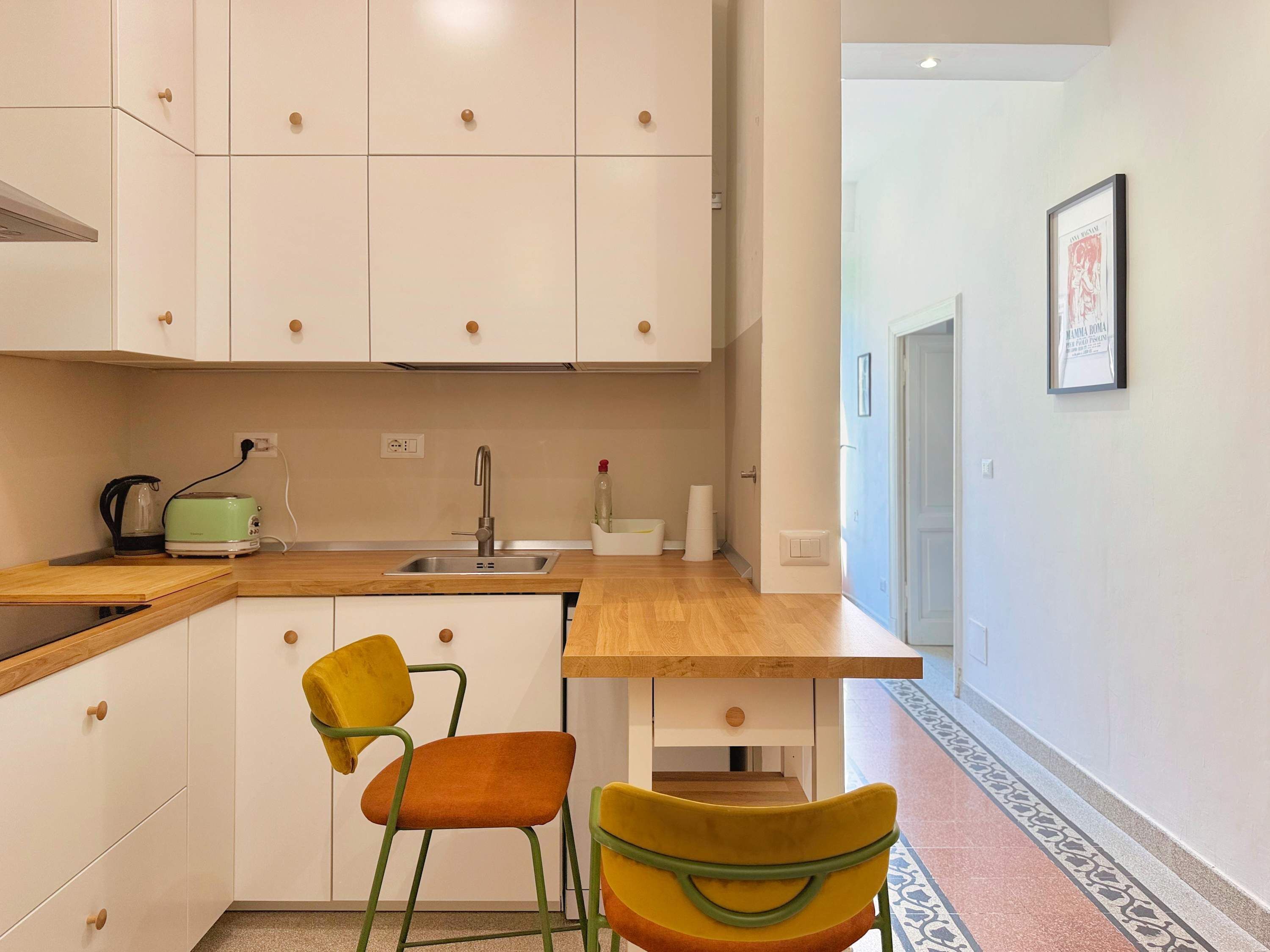 Una cucina moderna con mobili bianchi, un piano di lavoro in legno e un lavello. Ci sono due sedie con rivestimento giallo e arancione.