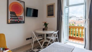 A hotel room with a bed, a small round table with chairs, a potted plant, and a TV on the wall. - Rampa Brancaleone Charming Apartment With View (Rome)