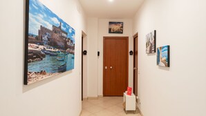 A hallway with a large painting of a coastal scene, a wooden door, and a small table with a red book. - Cloud Swing Apartment by Wonderful Italy (Bari)