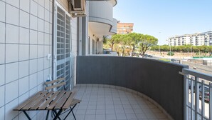 A balcony with a wooden bench, tiled floor, and a view of a cityscape with buildings and trees. - Cloud Swing Apartment by Wonderful Italy (Bari)