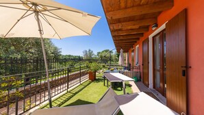 Un balcon avec une table et des chaises, un grand parasol et une vue sur un jardin et des arbres.