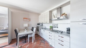 Une cuisine compacte avec des meubles blancs, une cuisinière à gaz, un four à micro-ondes et un évier. On y trouve une table à manger avec des chaises et une petite plante posée sur le comptoir.