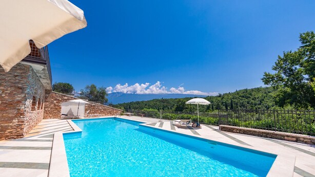Une piscine bordée d’un mur en pierre, avec vue sur une colline boisée.