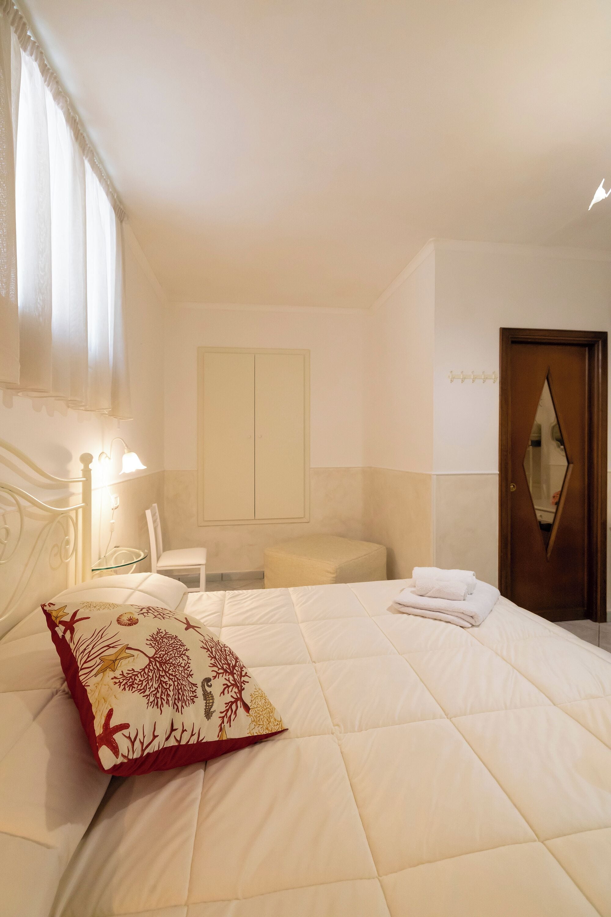 A hotel room with a bed, a chair, a small table, and a door with a mirror.