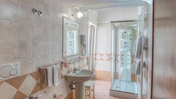 Un baño con ducha de vidrio, lavamanos sobre pedestal y tocador con espejo.