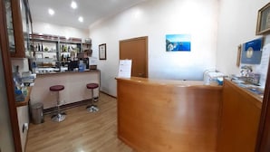 A reception area with a wooden counter, two bar stools, a door, and a wall-mounted sign. - Le Marelle  (Furore)