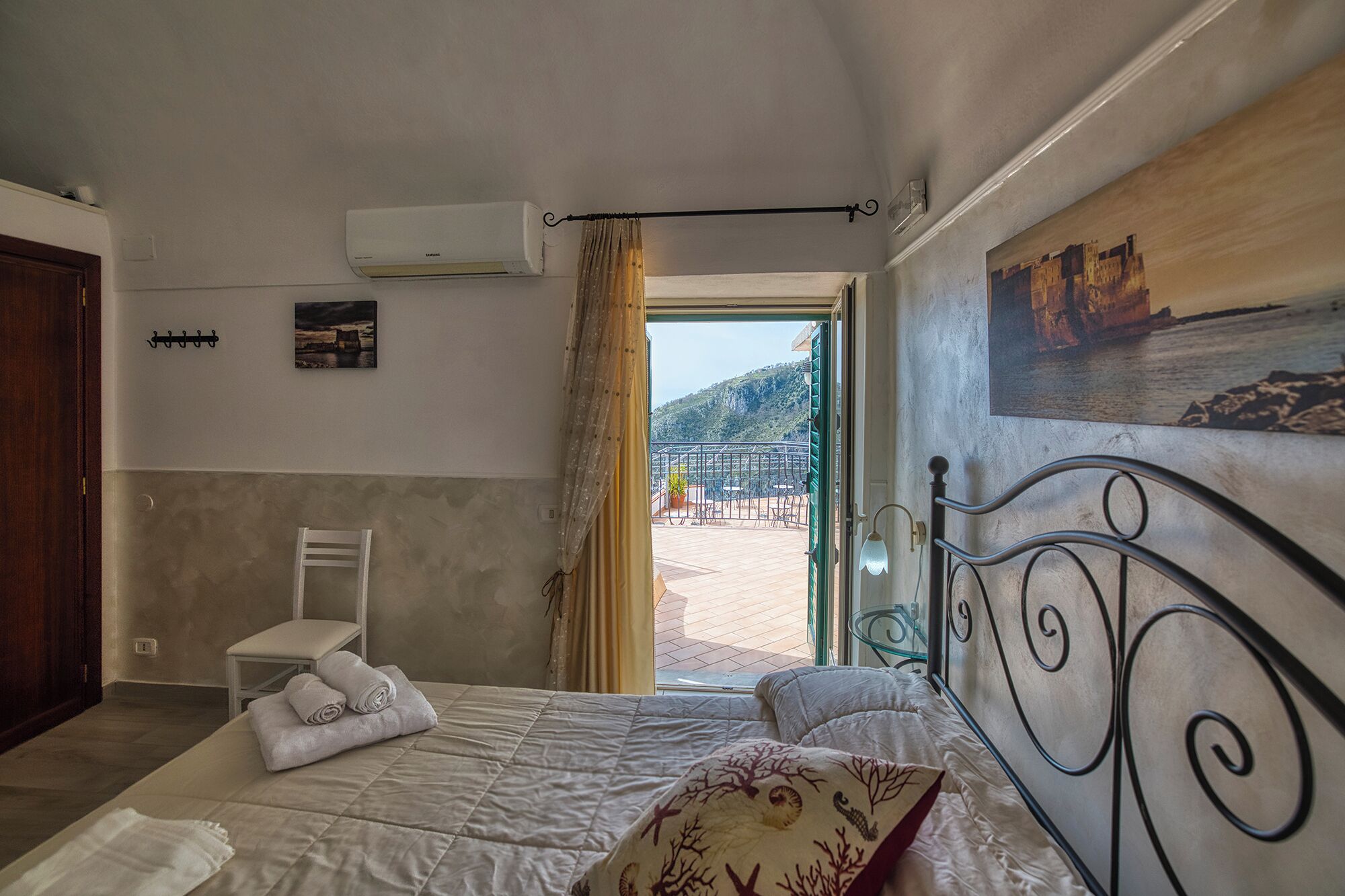 A bedroom with a bed, a chair, a painting, and an air conditioning unit.