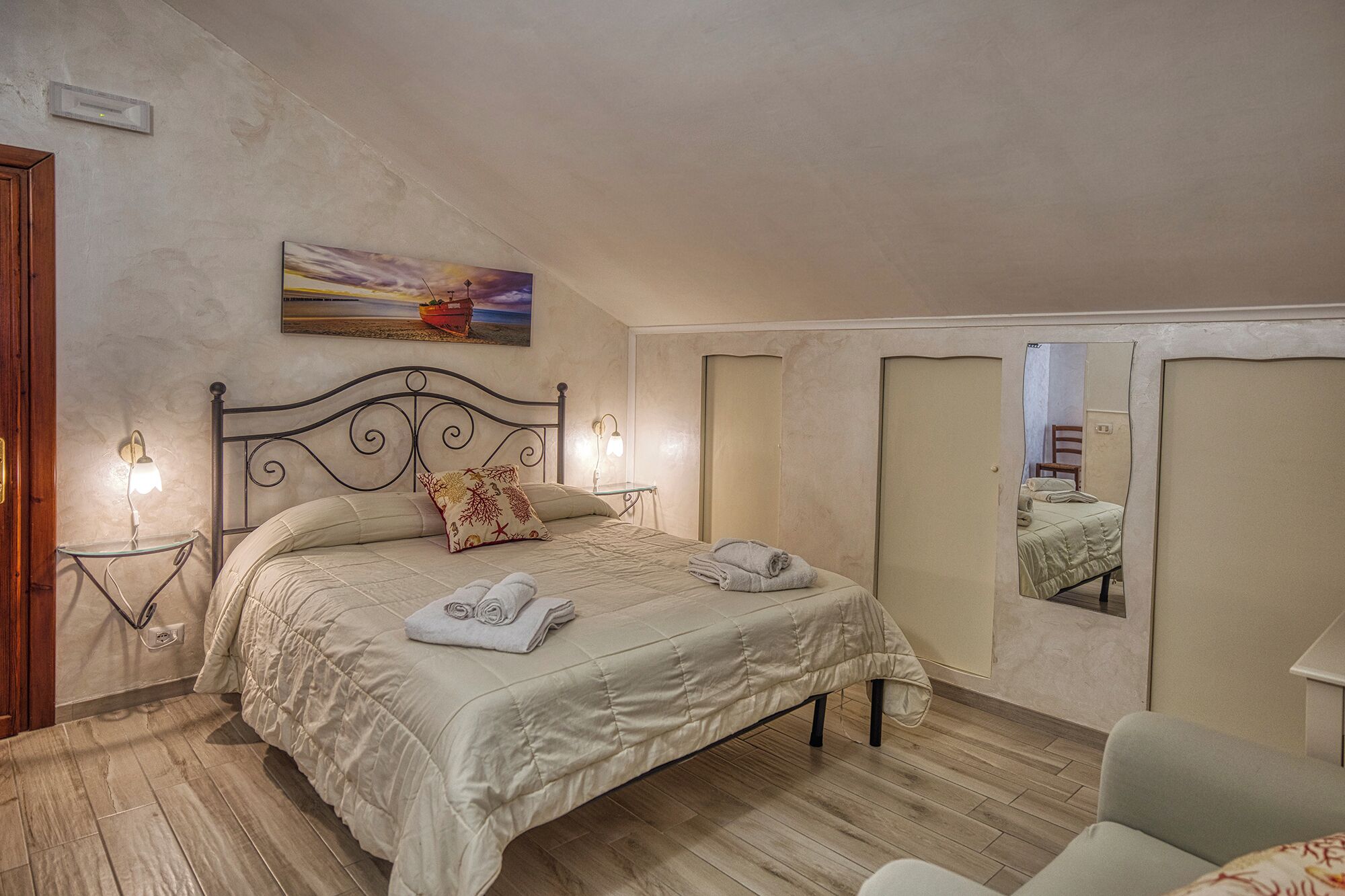 A bedroom with a bed, bedside lamps, a painting, and a mirror.