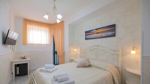 A hotel room with a bed, a TV mounted on the wall, a painting of a sunset, and a window with curtains. - Le Marelle  (Furore)