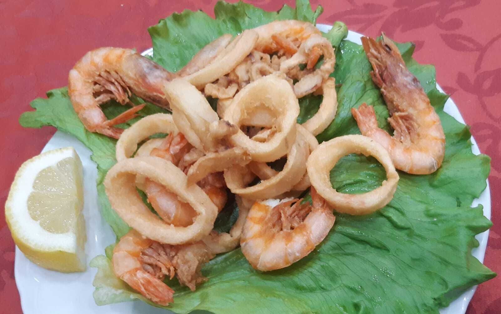 A plate of fried seafood, including shrimp and squid rings, served on a bed of lettuce with a lemon wedge.