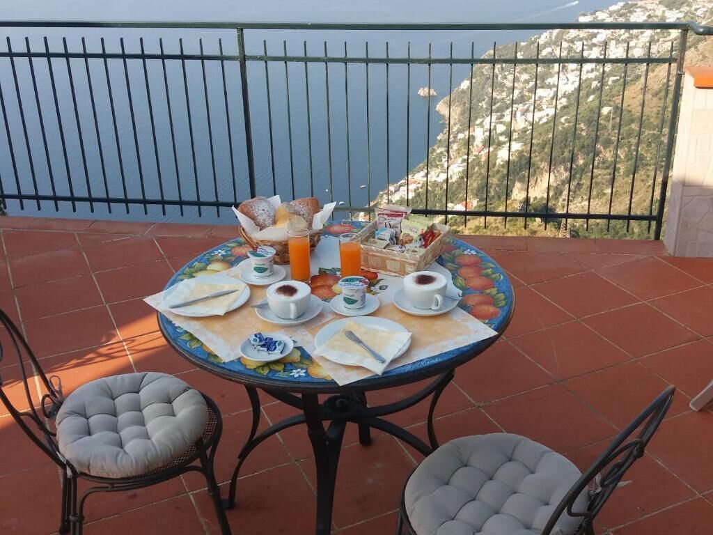 A round table with breakfast items on a terrace with a view of the sea and mountains.