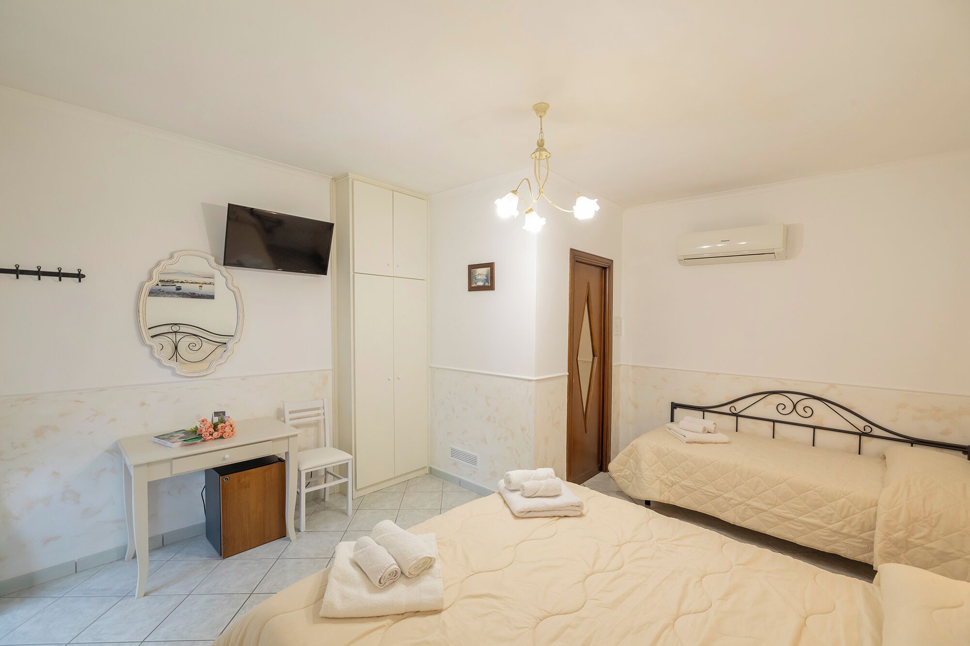 A bedroom with a bed, a desk, a chair, a TV, and an air conditioning unit.