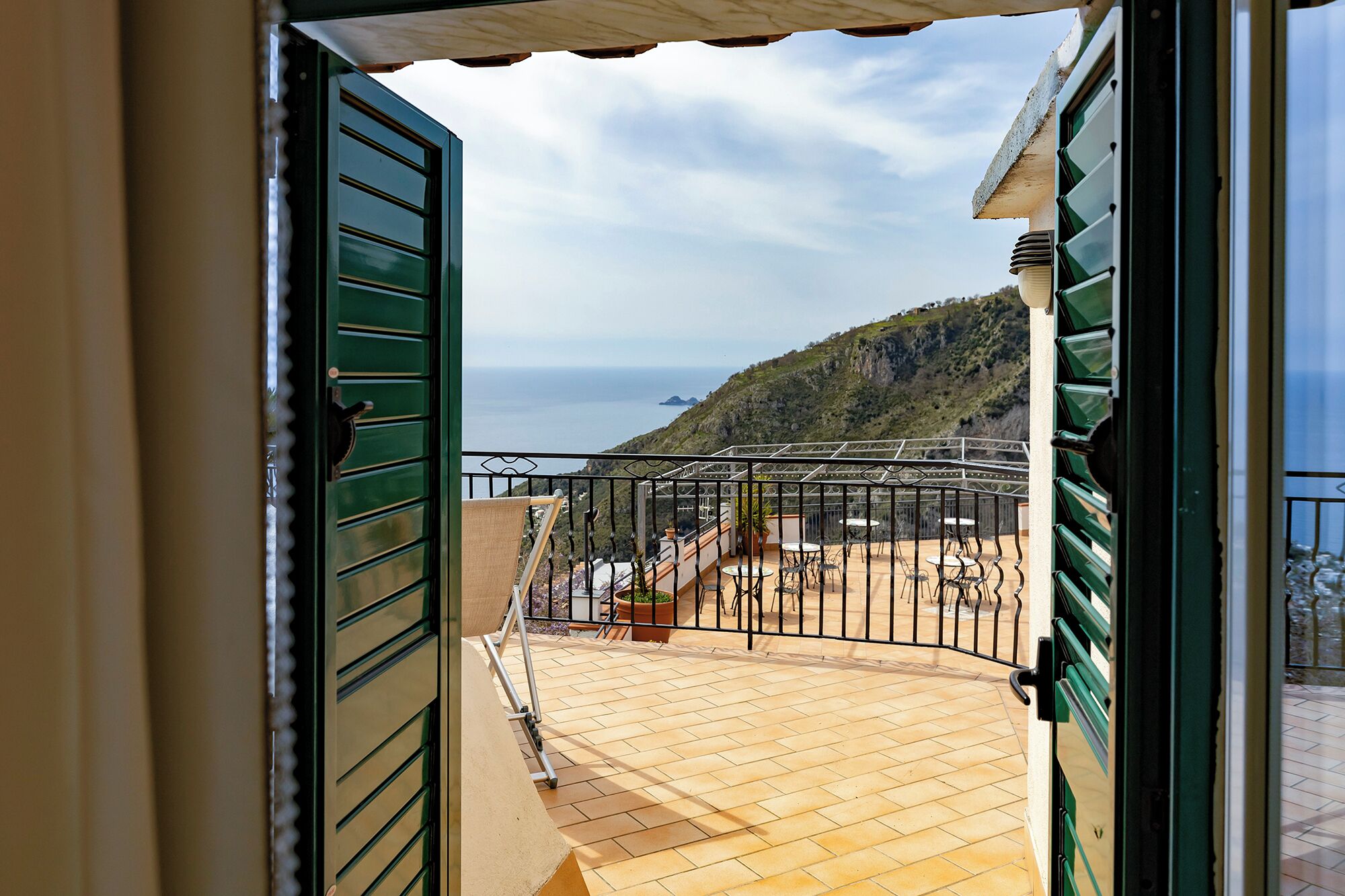 A balcony with a view of the sea and a hilly landscape.
