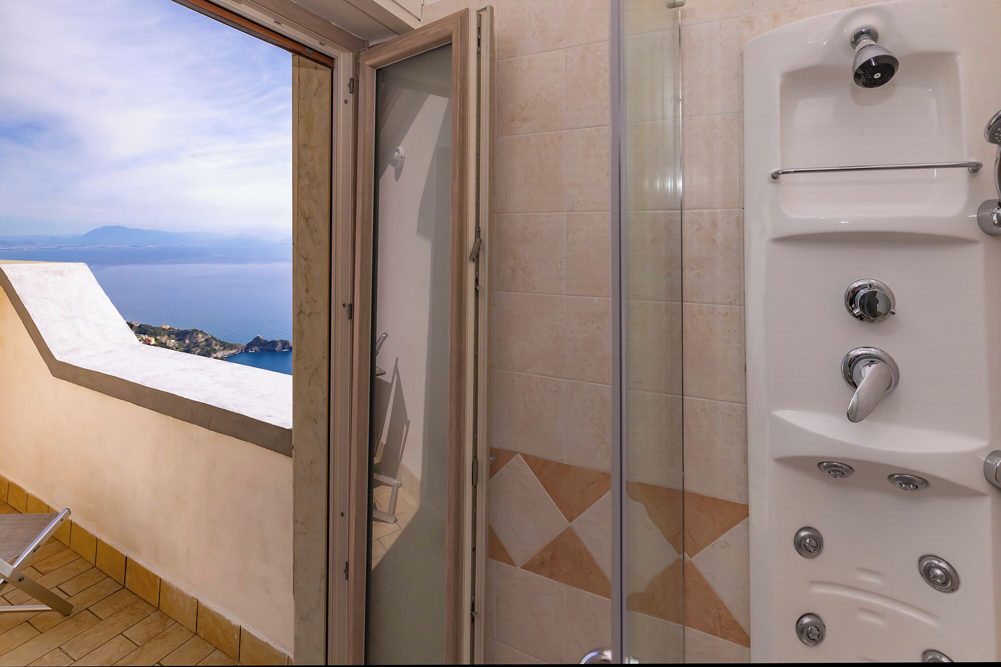 Een badkamer met een douchecabine van glas, een bad en uitzicht op zee.