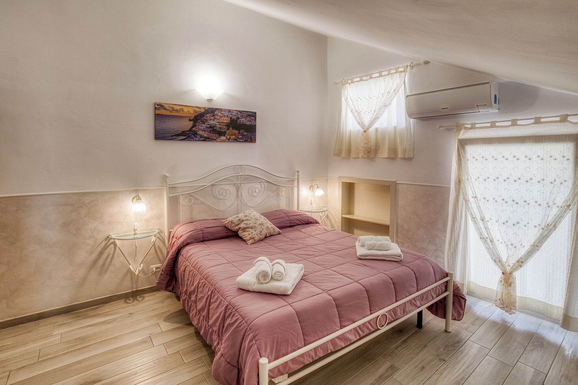 Un dormitorio con cama, lámparas de noche, mesita de noche, aire acondicionado de pared y ventana con cortinas.