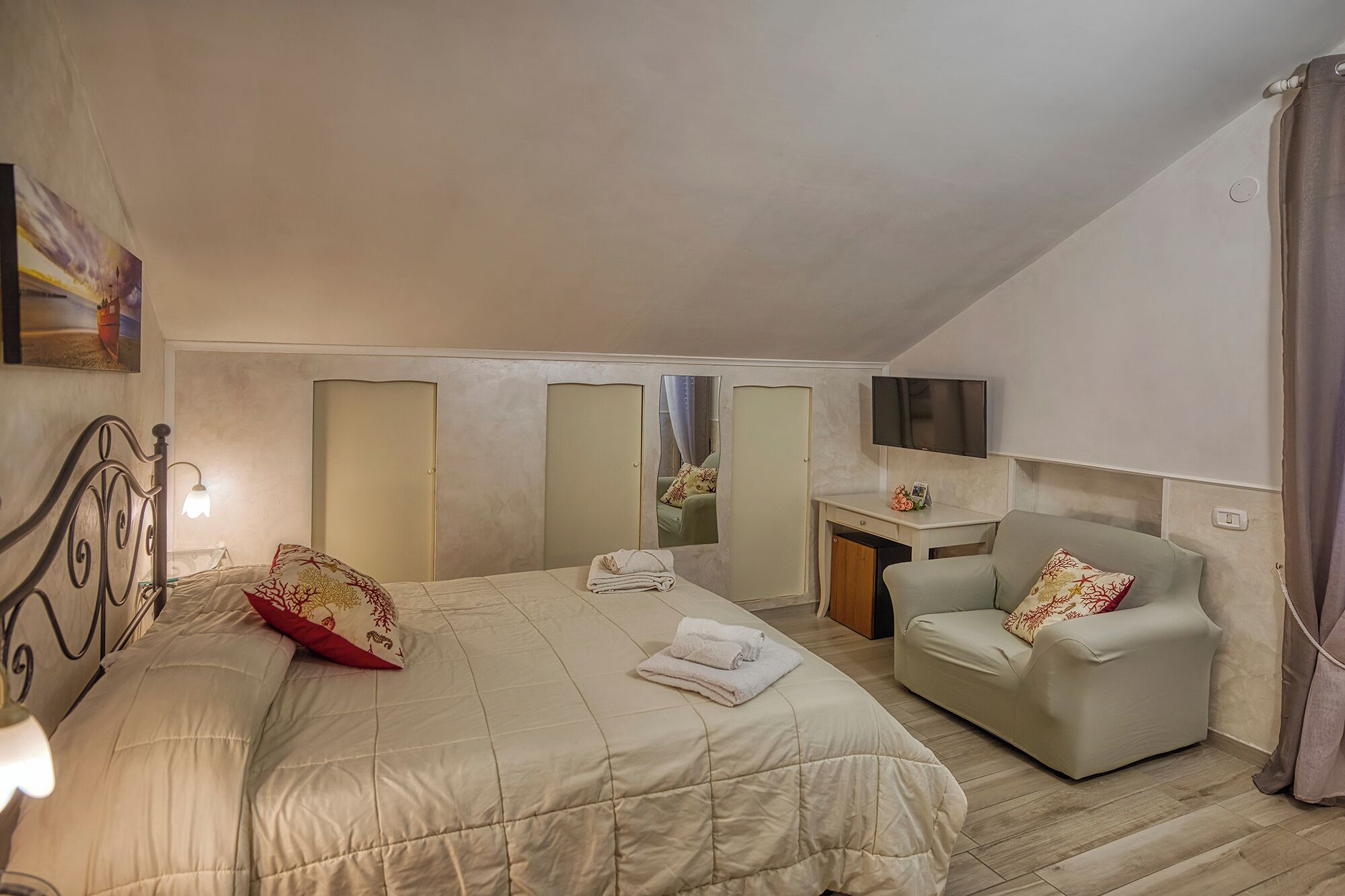 A bedroom with a bed, a chair, a desk, a mirror, and a TV.