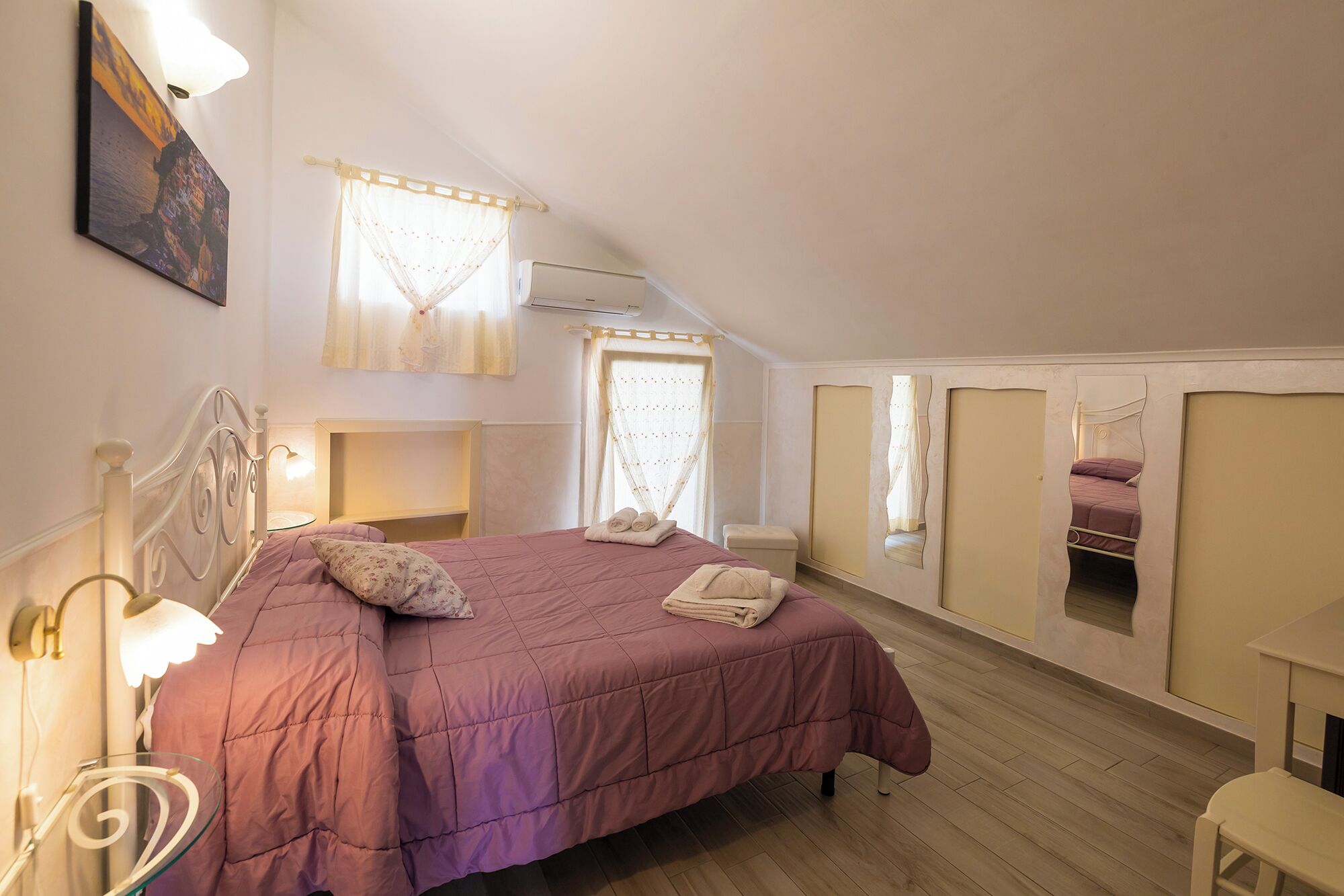 A bedroom with a large bed, a bedside table, a mirror, and a window with curtains.