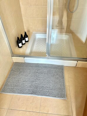 Uma área de chuveiro com porta de vidro, tapete de banho e três frascos de shampoo.