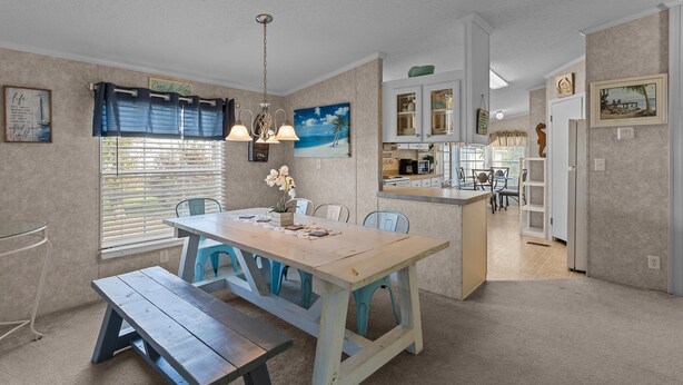 A dining area with a wooden table and benches, a kitchen with white cabinets, and a view of the beach through the window. - Clari's Place: 6mins to Holden Beach/Pets/Boat Parking/Plenty of Coastal Charm! (Supply)