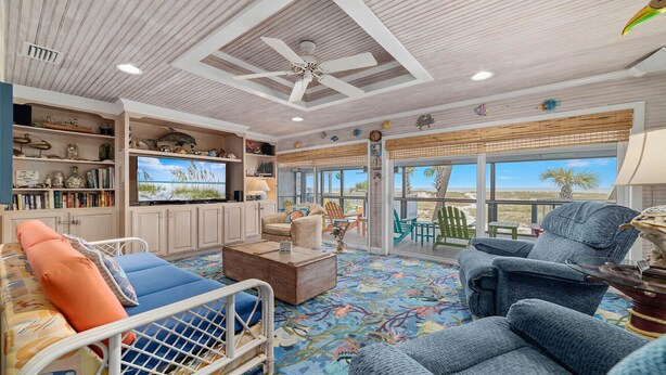 Ein großzügiges Wohnzimmer mit einem großen Fernseher, bequemen Sitzgelegenheiten und Blick auf den Strand.