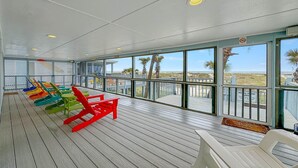 Eine überdachte Terrasse mit bunten Adirondack-Stühlen, große Fenster mit Blick auf den Strand und Palmen.
