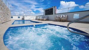 A rooftop pool area with two hot tubs, lounge chairs, and a stone wall. - Cairns Central Getaway: A Sleek City Studio (Cairns)