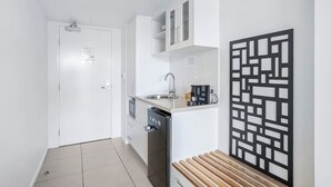 A compact kitchen with white cabinetry, a dishwasher, a sink, and a decorative black panel on the wall. - Cairns Central Getaway: A Sleek City Studio (Cairns)