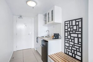 Une cuisine compacte avec des meubles blancs, un lave-vaisselle, un évier et un panneau noir décoratif sur le mur.