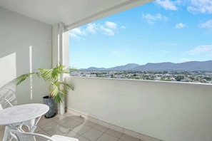 Un balcone con vista sulla città e sulle montagne, un tavolo bianco e una pianta in vaso.
