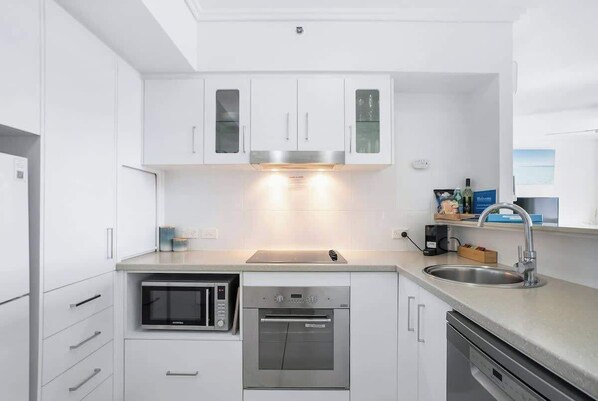 A modern kitchen with white cabinetry, a built-in microwave, an oven, and a dishwasher. - Cairns City Escape—Elevated Modern Haven with Pool (Cairns)