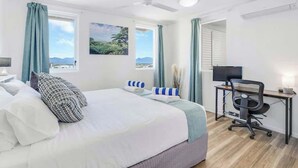 Ein Schlafzimmer mit einem Bett, einem Schreibtisch, einem Stuhl, einem Deckenventilator und einem Fenster mit Vorhängen.