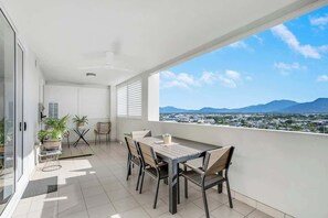 Un balcone con tavolo e sedie, piante in vaso e vista sulla città e sulle montagne.