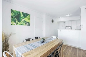 A modern dining area with a wooden table, chairs, and a kitchen in the background.