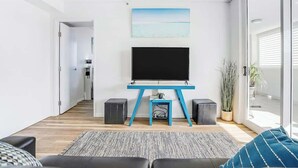 Ein modernes Wohnzimmer mit einem Flachbildfernseher auf einem blauen Standfuß, einer Couch, einem gemusterten Teppich und einem Blumentopf.